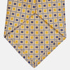 View 3 of product The Turnbull & Asser Yellow and Navy Geometric Silk Jacquard Tie features a striking square pattern on a light background, ideal for formal occasions, shown rolled up against a plain white surface.