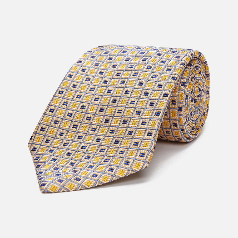 The Turnbull & Asser Yellow and Navy Geometric Silk Jacquard Tie features a striking square pattern on a light background, ideal for formal occasions, shown rolled up against a plain white surface.