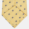 View 3 of product The Turnbull & Asser Yellow Fine Square Slub Silk Tie features a soft yellow jacquard with a subtle texture, decorated with a repeating blue and white diamond pattern, shown rolled up on a plain white background.