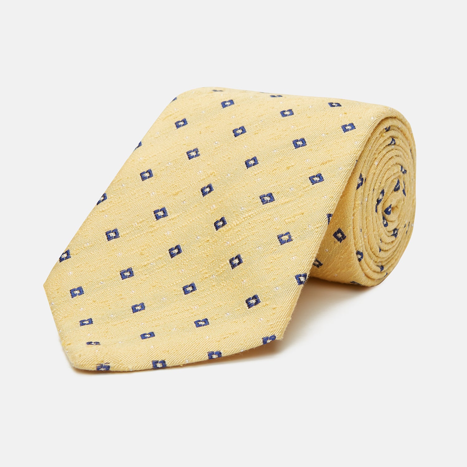 View 1 of product The Turnbull & Asser Yellow Fine Square Slub Silk Tie features a soft yellow jacquard with a subtle texture, decorated with a repeating blue and white diamond pattern, shown rolled up on a plain white background.