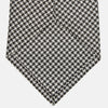 View 3 of product The Turnbull & Asser Fine Puppytooth Monochrome Silk Tie, in classic black and white, features a refined pattern and is shown rolled on a plain white background—ideal for enhancing any formal outfit.