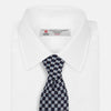 View 4 of product The Turnbull & Asser Indigo Graphic Floral Silk Jacquard Tie features a repeating pattern of light blue and white geometric shapes, shown rolled up on a plain white background.