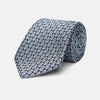 View 1 of product The Chambray Blue Graphic Floral Silk Jacquard Tie by Turnbull & Asser features a modern floral pattern in silk, shown rolled up against a plain white background.