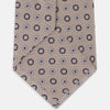 View 4 of product The Turnbull & Asser Beige Spheric Emblem Tie, a formalwear essential, features a neat roll and a repeating pattern of navy and white circular floral motifs on pastel beige.