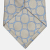 View 3 of product The Turnbull & Asser Toffee and Powder Blue Circle Jacquard Silk Tie, featuring an interlocking circular pattern, is rolled up and displayed on a plain white background.