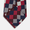 View 4 of product The Burgundy Checkerboard Silk Jacquard Tie by Turnbull & Asser features a bold autumnal pattern in red, navy blue, brown, gray, burgundy, and white squares, shown rolled on a plain white background.
