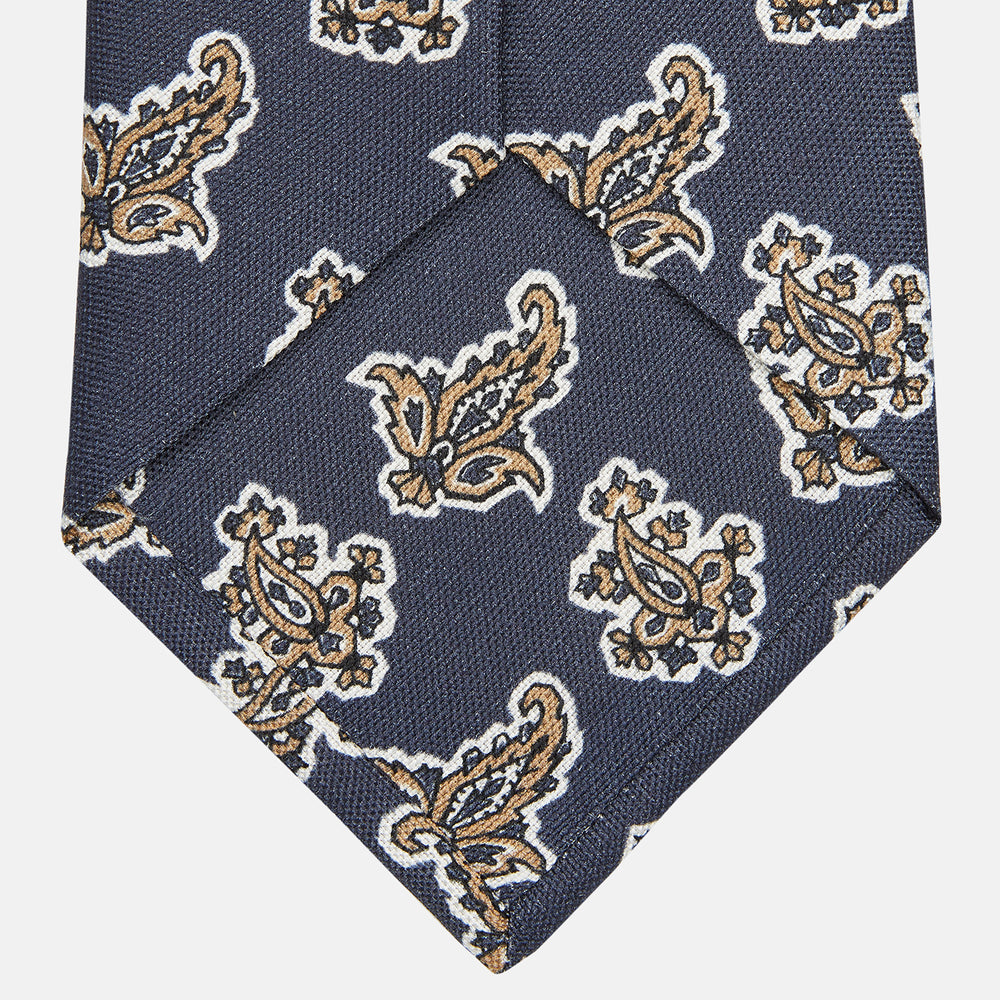 The Turnbull & Asser Navy Paisley Floral Cotton Silk Blend Tie features beige and light blue paisley motifs on navy, with one end rolled.