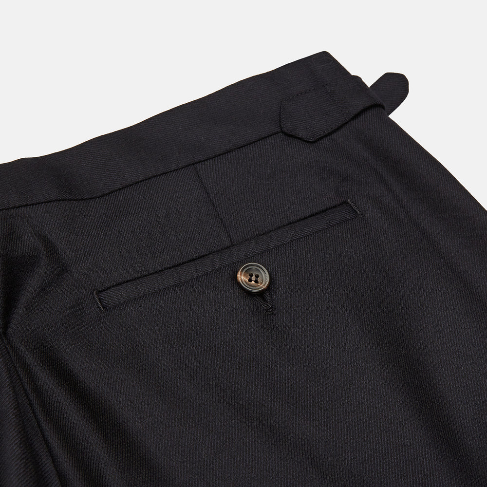 A pair of navy Escorial wool trousers by Turnbull & Asser, featuring a tailored style, straight-leg fit, front crease, belt loops, side pockets, and metal buckle details on the waistband, shown against a white background.