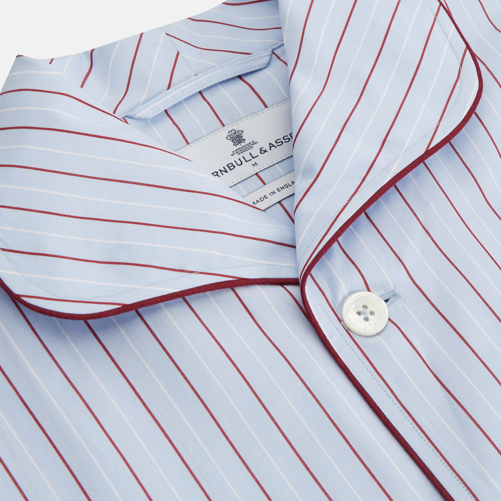 The Turnbull & Asser Burgundy Stripe Classic Pyjama Set features long sleeves, a button-up top with red piping, matching drawstring pants, and a traditional fit. Laid flat, it's luxury loungewear in signature burgundy stripes.