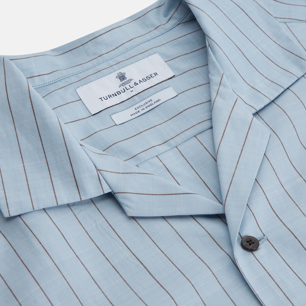 Turnbull & Asser's Pale Blue Stripe Cotton Holiday Fit Shirt features a revere collar, thin black pinstripes, single button cuff, chest pocket, and black buttons—crafted from Italian cotton and laid flat on a white background.