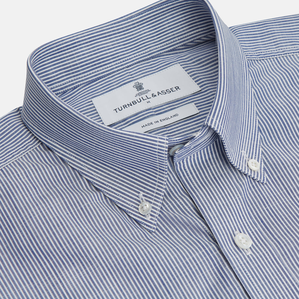 Turnbull & Asser’s Indigo Chambray Stripe Weekend Fit Shirt with Dorset collar features thin white pinstripes, two button-flap chest pockets, buttoned cuffs, and relaxed styling—presented flat on a white background.