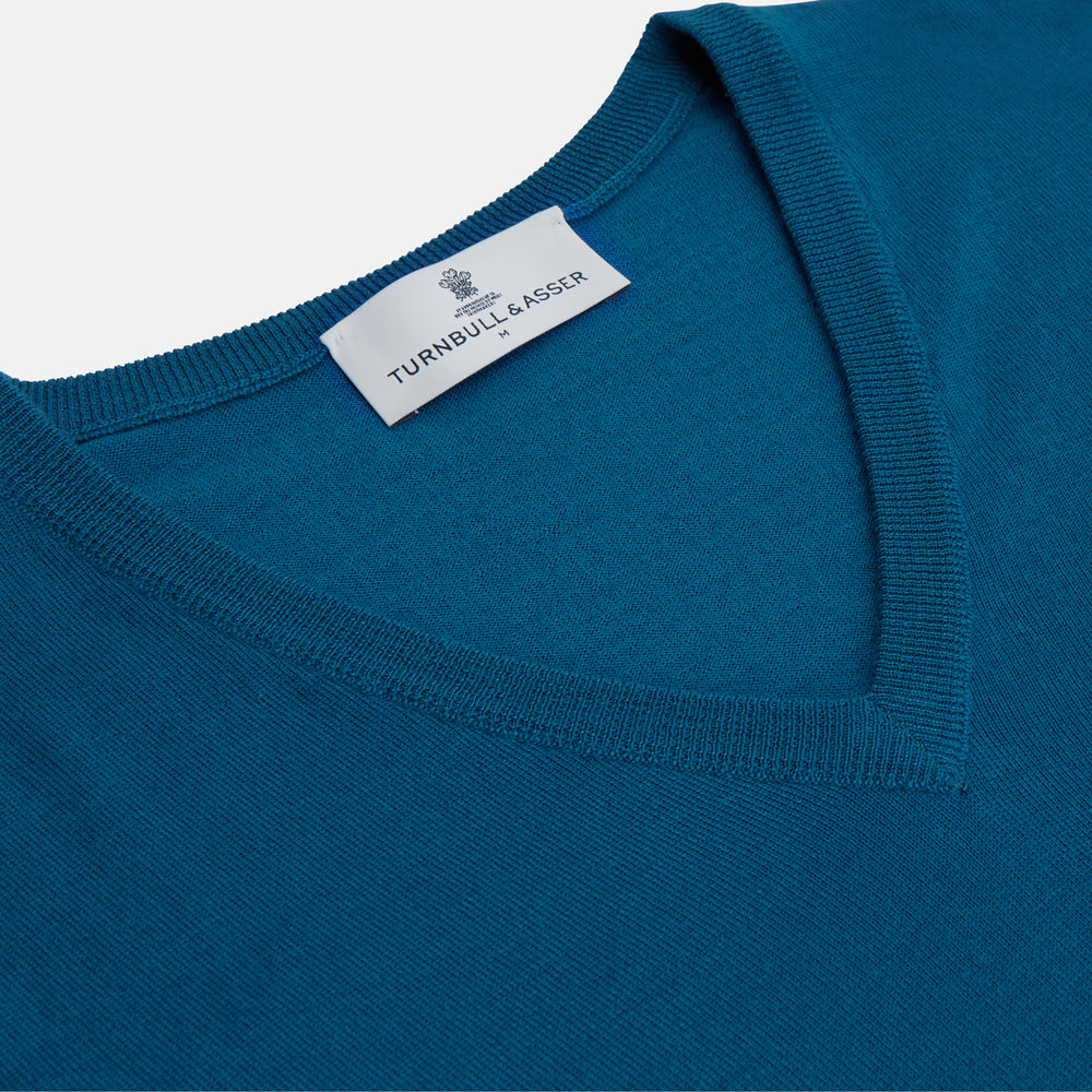 The Turnbull & Asser Ocean Blue Merino Kennedy V-Neck Jumper, shown flat on a white background, features ribbed cuffs and hem with a visible branded label at the neckline.