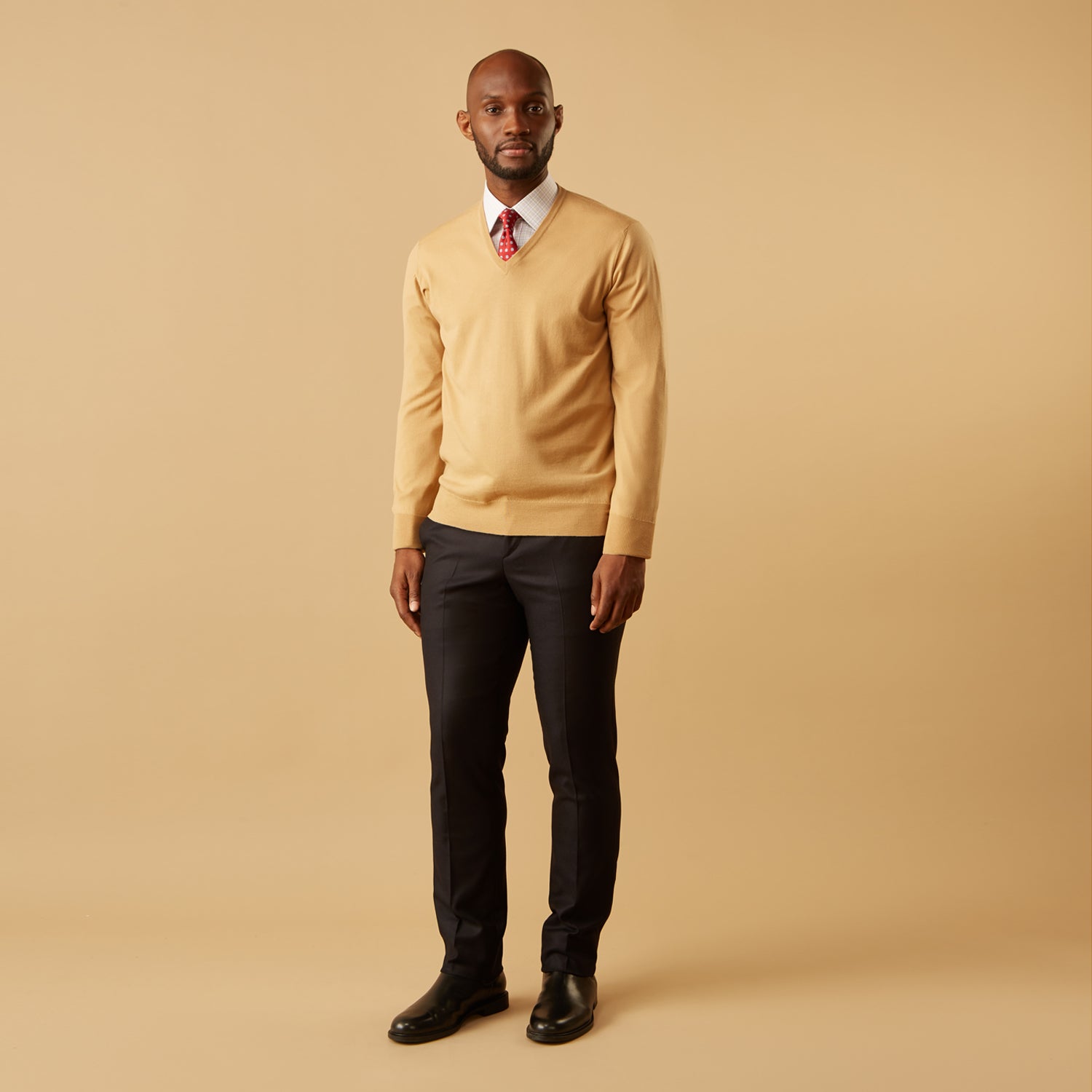 View 3 of product The Turnbull & Asser Camel V-Neck Merino Wool Jumper, with ribbed cuffs and a visible white neckline label, is neatly folded with one sleeve showing—an essential, versatile staple for any gentleman's wardrobe.