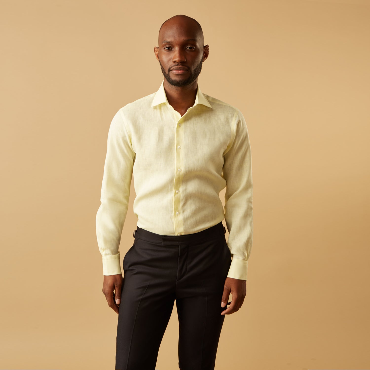 View 1 of product A man stands against a beige background, wearing the Turnbull & Asser Cream Tailored Fit Shelton Shirt with a Kent collar and black pants. He faces forward with a neutral expression, his arms relaxed by his sides.