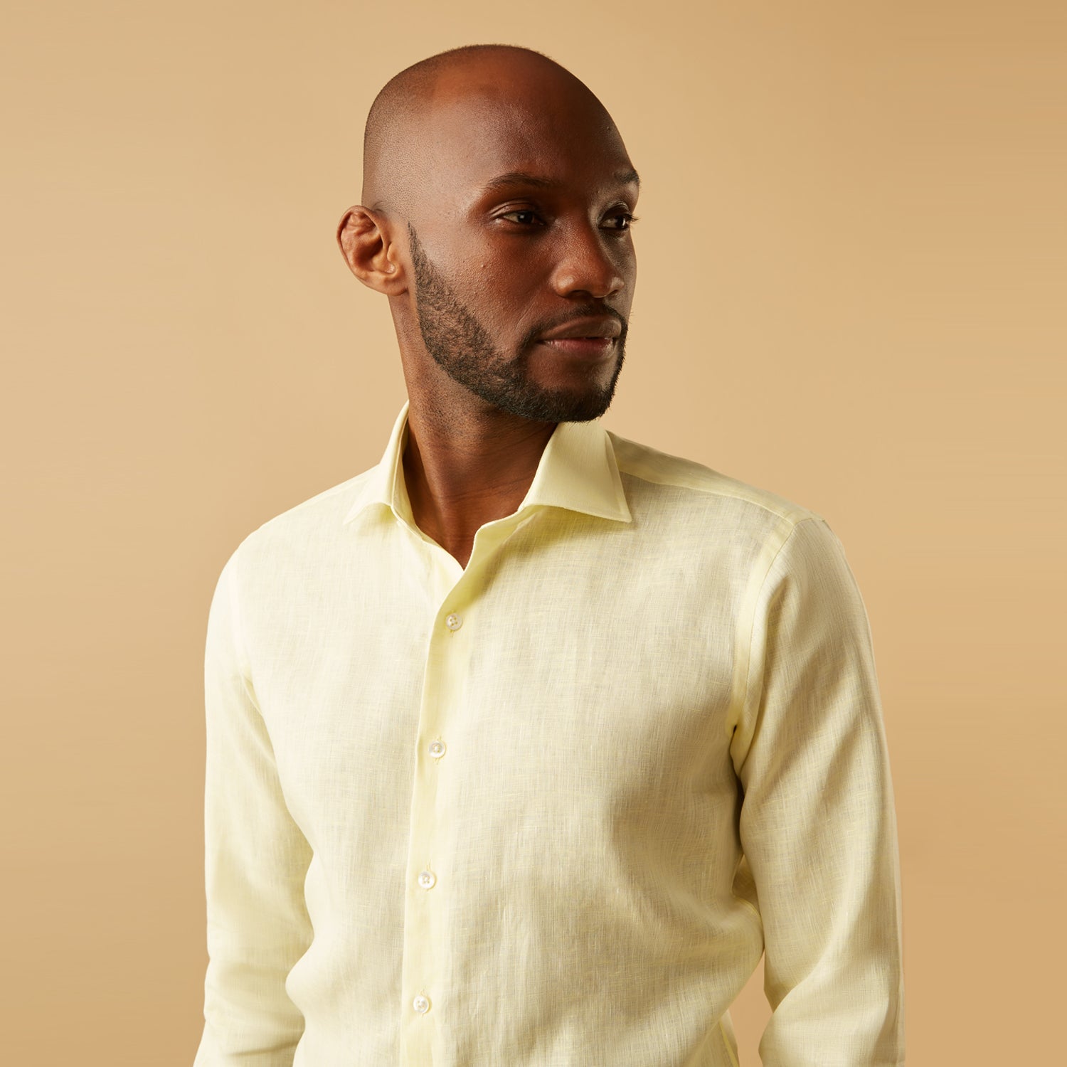 View 3 of product A man stands against a beige background, wearing the Turnbull & Asser Cream Tailored Fit Shelton Shirt with a Kent collar and black pants. He faces forward with a neutral expression, his arms relaxed by his sides.