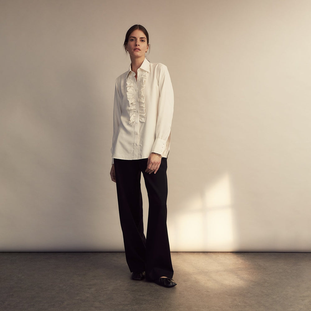 The Turnbull & Asser Turnbull and The Deck Cream Silk Romantic Shirt features long sleeves, a pointed collar, and elegant front ruffles, shown against a plain light gray background.
