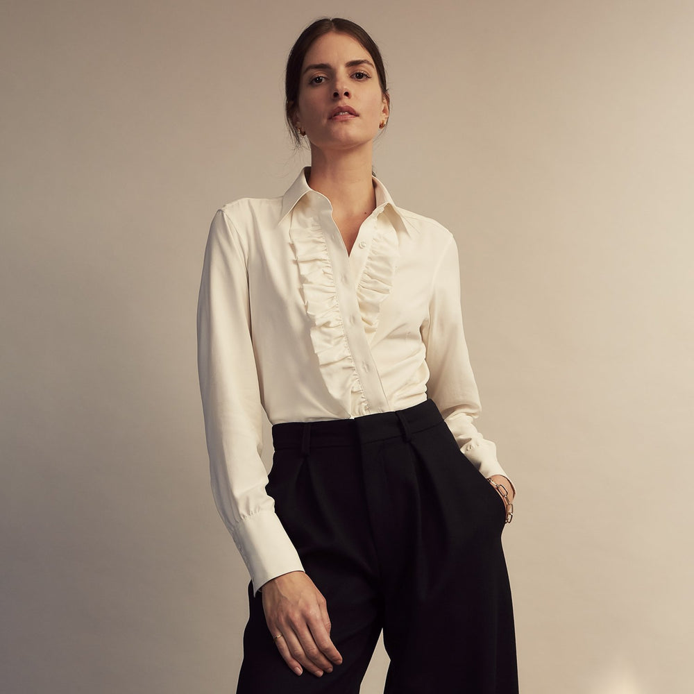 The Turnbull & Asser Turnbull and The Deck Cream Silk Romantic Shirt features long sleeves, a pointed collar, and elegant front ruffles, shown against a plain light gray background.