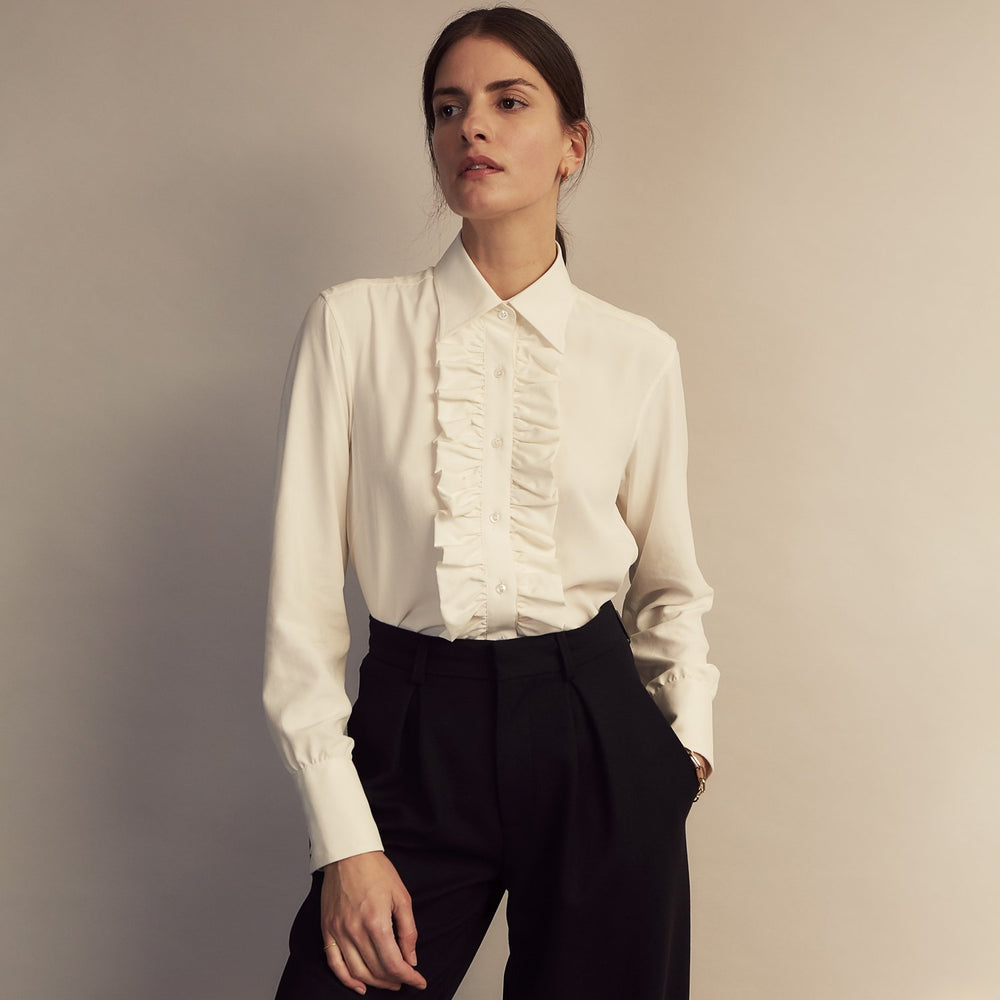 The Turnbull & Asser Turnbull and The Deck Cream Silk Romantic Shirt features long sleeves, a pointed collar, and elegant front ruffles, shown against a plain light gray background.