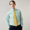 View 3 of product A man stands against a plain background, wearing a Turnbull & Asser Green Fine Stripe Regular Fit Shirt with a T&A collar, paired with a yellow tie, dark trousers, and black shoes. He looks slightly left with his hands at his sides.
