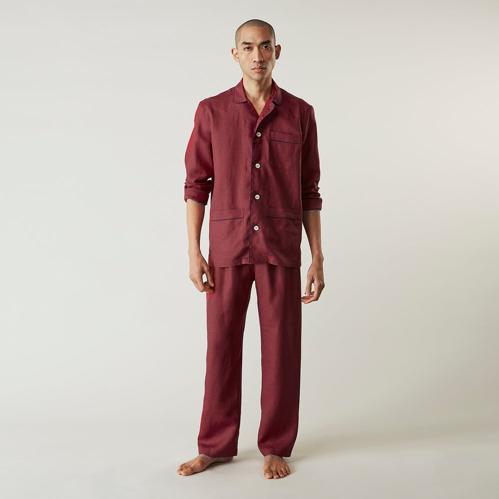 The Turnbull & Asser Burgundy Linen Modern Pyjama Set features a button-up, collared long-sleeve top with black piping and three pockets, plus matching pants with an elastic waistband.