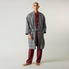 View 1 of product A barefoot person wears Turnbull & Asser's Navy Silk Chequered Kimono Gown with a belt over maroon pyjama sets, standing against a plain light background.