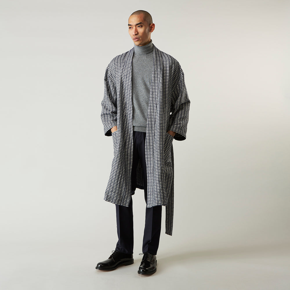 A barefoot person wears Turnbull & Asser's Navy Silk Chequered Kimono Gown with a belt over maroon pyjama sets, standing against a plain light background.