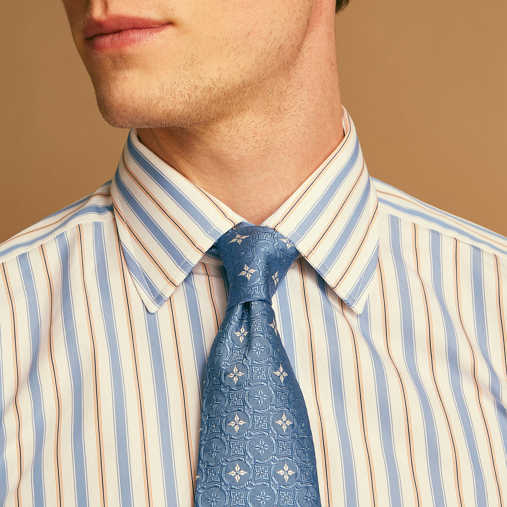 The Blue Multi Neat Silk Tie by Turnbull & Asser features a geometric pattern of white four-pointed shapes and circles, crafted in blue silk from the autumn-winter collection. Displayed rolled on a plain light background.