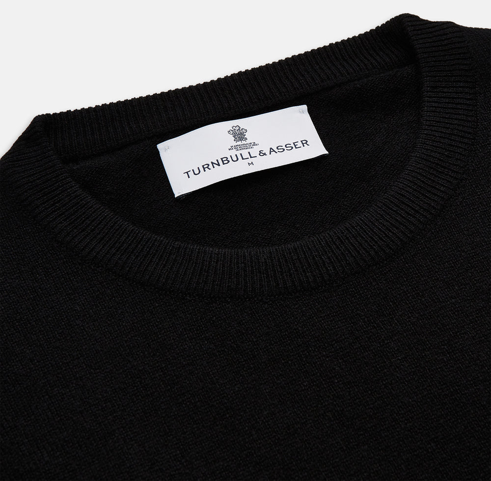 The Turnbull & Asser Black Crew Neck Cashmere Jumper is shown laid flat on a white background, featuring ribbed cuffs and hem with a small white label inside the collar.