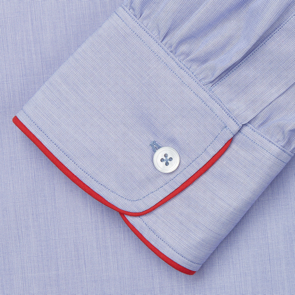 The Blue Piped End-on-End Cotton Nightshirt by Turnbull & Asser features light blue cotton, red piped accents, a chest pocket, high-low hem, and half-button placket—luxurious nightwear inspired by classic nightshirt style.
