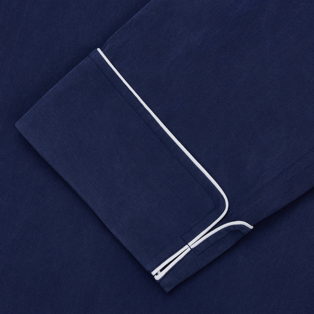 The Turnbull & Asser Navy Piped Silk Pyjama Set features a long-sleeve button-up top with a chest pocket and matching drawstring pants, laid flat on a white background for a luxurious look.