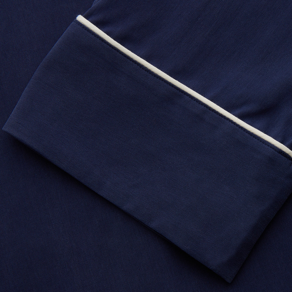 The Women's Harriet Navy Silk Pyjama Set by Turnbull & Asser features a long-sleeve, button-up top with white piping and chest pocket, plus matching drawstring pants—luxurious sleepwear displayed on a white background.