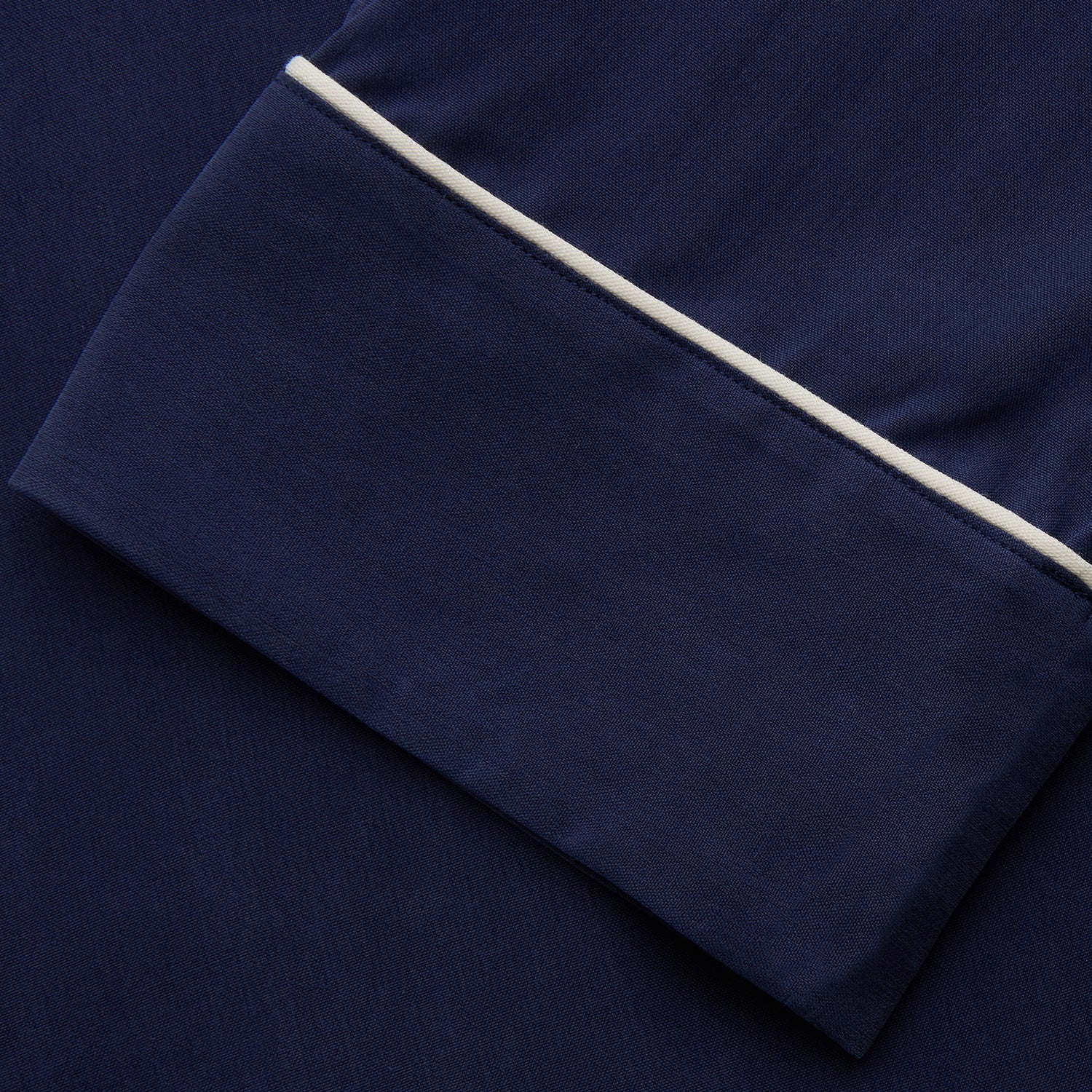 View 4 of product The Women's Harriet Navy Silk Pyjama Set by Turnbull & Asser features a long-sleeve, button-up top with white piping and chest pocket, plus matching drawstring pants—luxurious sleepwear displayed on a white background.