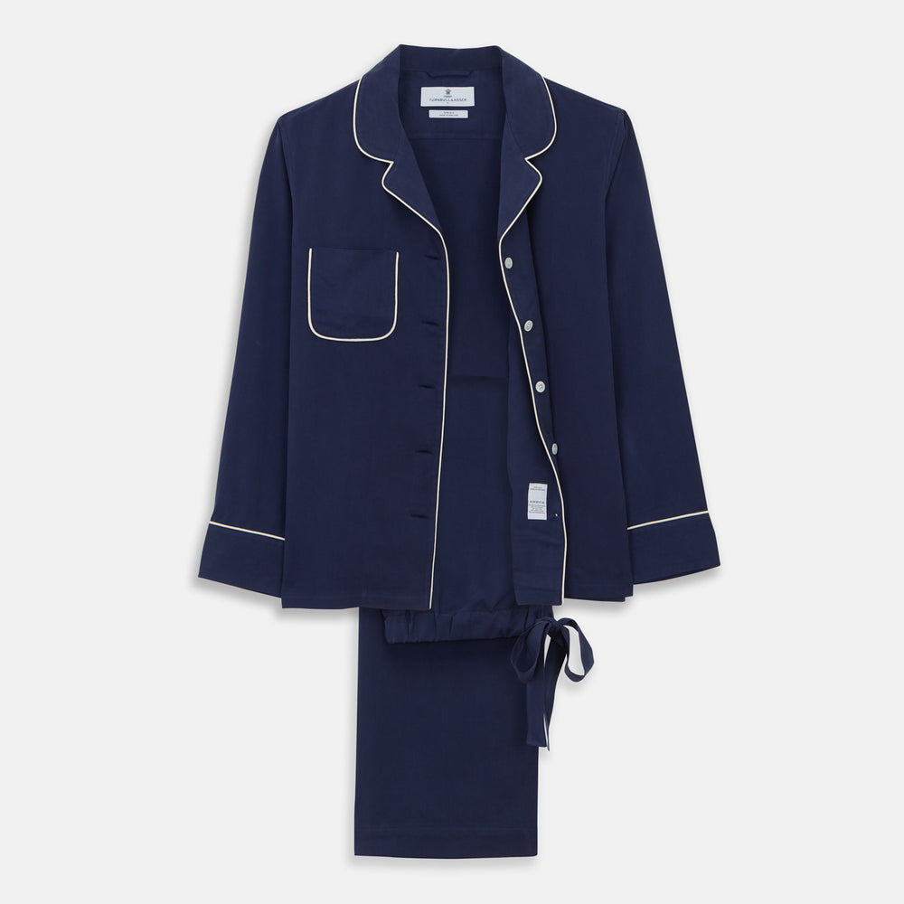 The Women's Harriet Navy Silk Pyjama Set by Turnbull & Asser features a long-sleeve, button-up top with white piping and chest pocket, plus matching drawstring pants—luxurious sleepwear displayed on a white background.