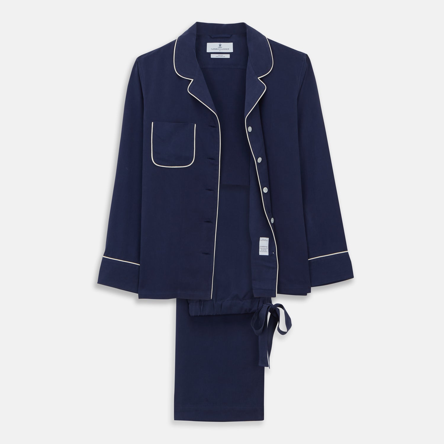 View 1 of product The Women's Harriet Navy Silk Pyjama Set by Turnbull & Asser features a long-sleeve, button-up top with white piping and chest pocket, plus matching drawstring pants—luxurious sleepwear displayed on a white background.