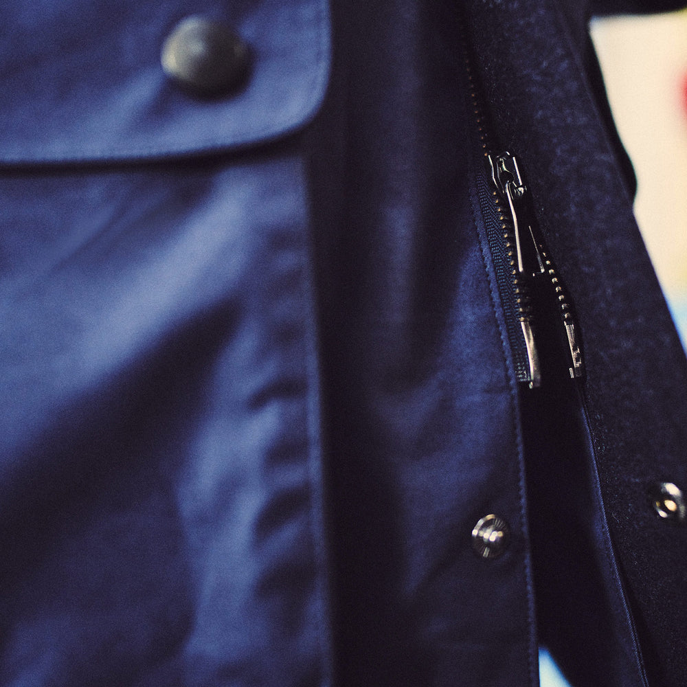 The Turnbull & Asser Navy Dry-Waxed Cotton Field Jacket features a collar, front zipper with snap buttons, two chest pockets, and large hip flap pockets, shown laid flat on a plain white background.