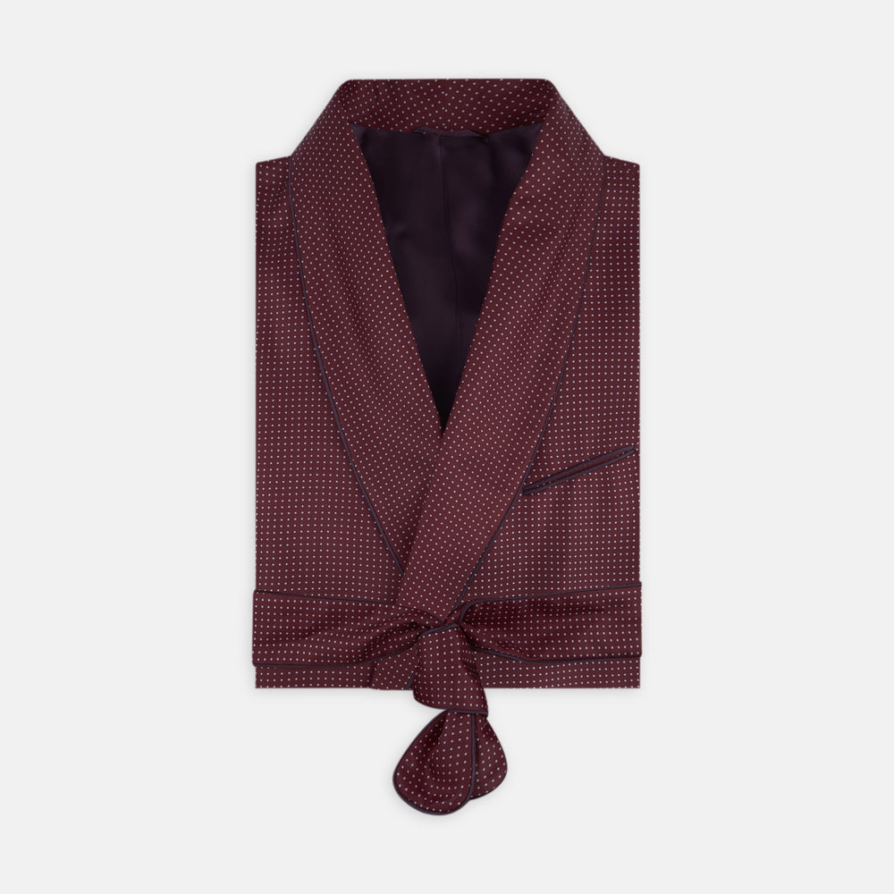 The Turnbull & Asser Burgundy Piped Silk Spot Gown features small white polka dots, a shawl collar, fabric belt, and chest pocket—luxurious nightwear and a stylish men’s statement piece—shown on a white background.