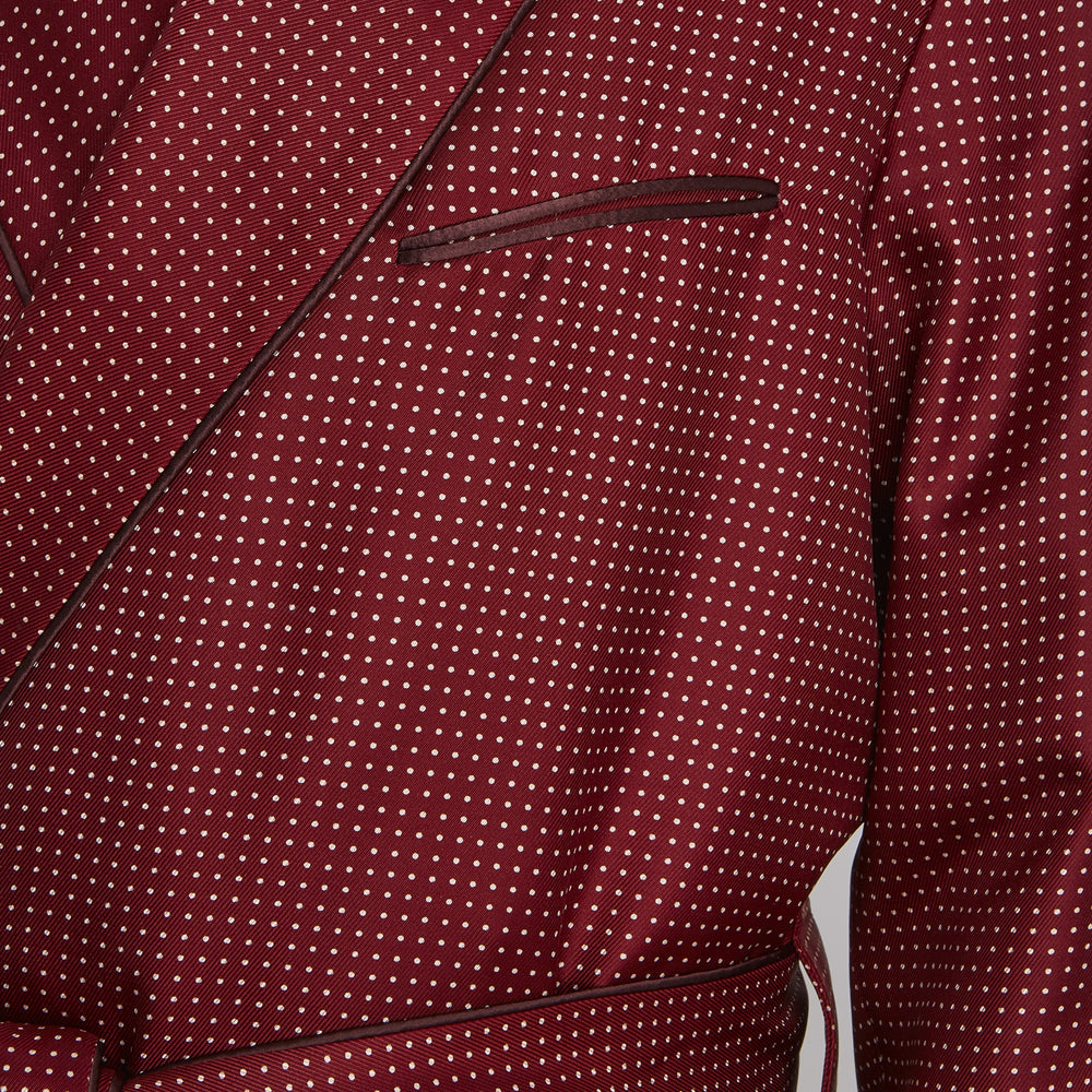 The Turnbull & Asser Burgundy Piped Silk Spot Gown features small white polka dots, a shawl collar, fabric belt, and chest pocket—luxurious nightwear and a stylish men’s statement piece—shown on a white background.