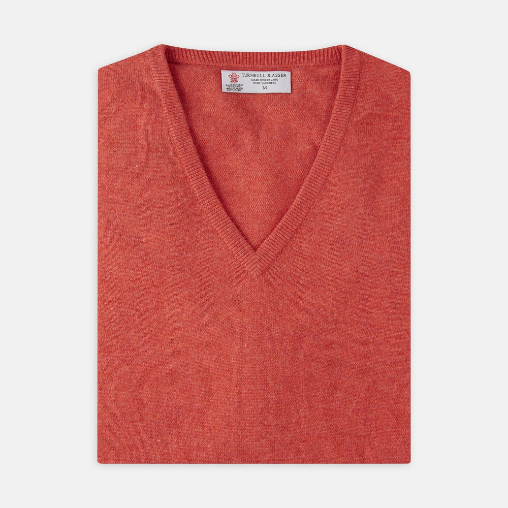 A folded Crimson Fine Cashmere Slipover by Turnbull & Asser in coral-red is shown against a white background, with the visible neckline label highlighting its premium Scottish cashmere quality.