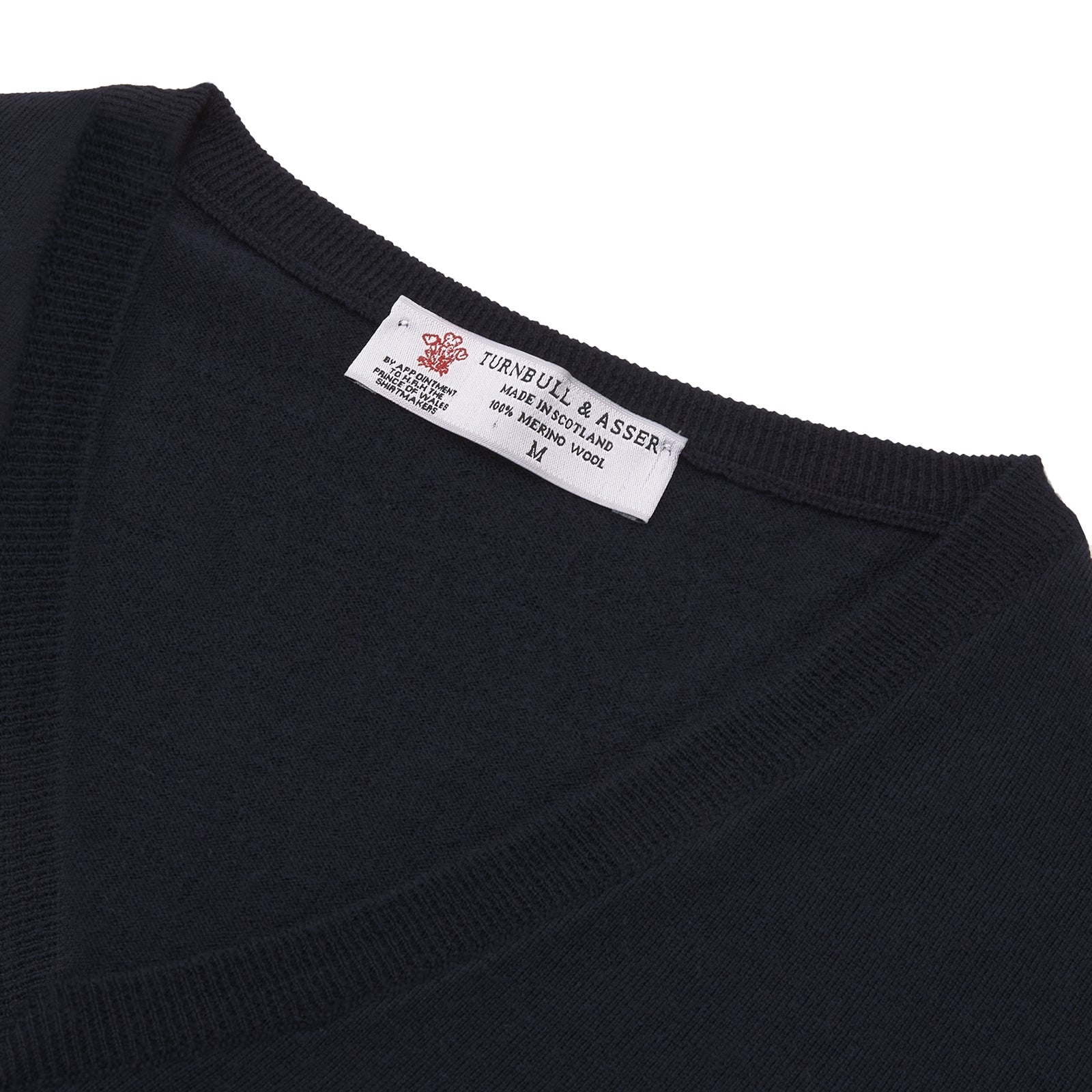 View 4 of product The Turnbull & Asser Indigo V-Neck Merino Wool Jumper, shown neatly folded with ribbed cuffs and a visible inner label, is a timeless essential in versatile navy, perfect for any gentleman’s wardrobe.