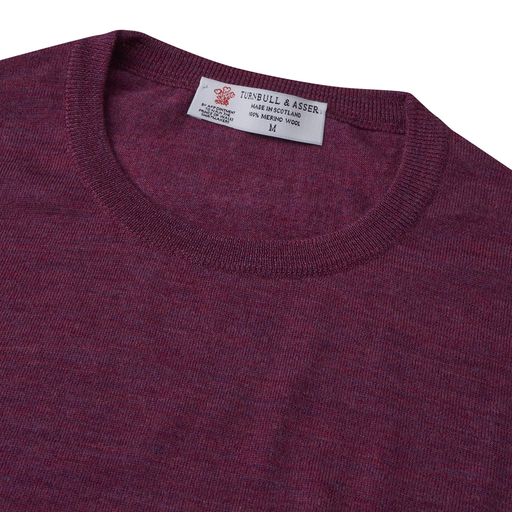 The Plum Fine Merino Crew Neck Jumper by Turnbull & Asser features classic Scottish knitwear craftsmanship in a rich maroon shade, shown neatly folded with long sleeves against a plain white background.