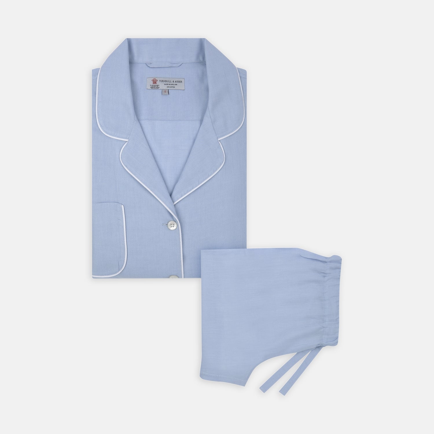 View 1 of product Turnbull & Asser Ladies' Blue Cotton-Cashmere Pyjama Set with white piping features a collared button-up top, neatly folded, and matching drawstring pants laid flat on a plain white background.