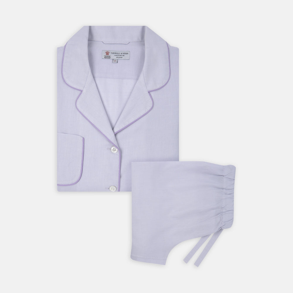 The Ladies' Lilac Cotton-Cashmere Pyjama Set by Turnbull & Asser, with purple piping, collared button-up top featuring a chest pocket, and matching drawstring bottoms, is folded and displayed on a white background.