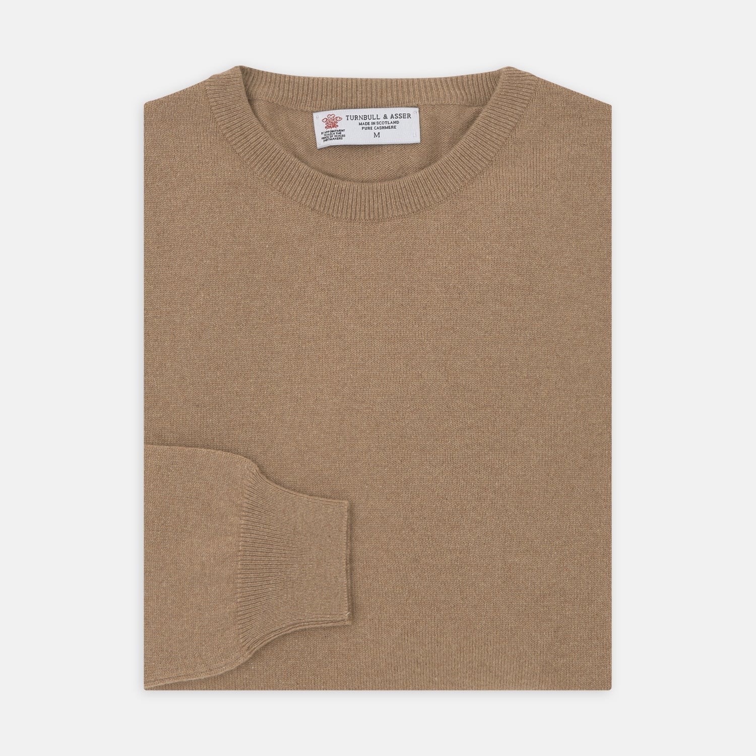 View 1 of product A folded Natural Crew Neck Cashmere Jumper by Turnbull & Asser, in light brown, features a visible brand label and one sleeve neatly laid across the front of this smart casual luxury Scottish sweater.