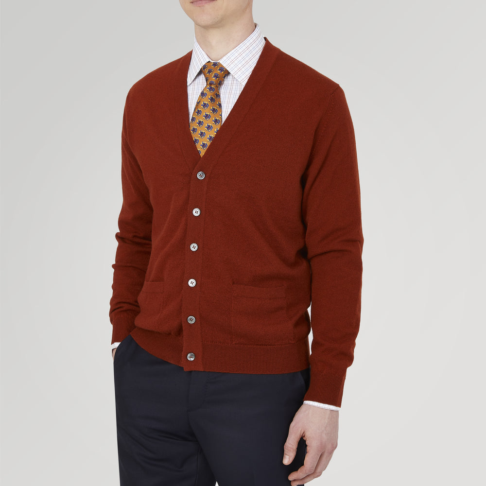 The Harissa Cashmere Cardigan by Turnbull & Asser, in deep red-brown 21GG knit, is folded to display its V-neck, ribbed cuffs, and two buttons against a white background.
