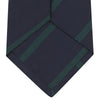 View 4 of product The Turnbull & Asser Navy and Green Blazer Stripe Repp Silk Tie features diagonal green stripes on navy silk, shown rolled at one end against a white background.