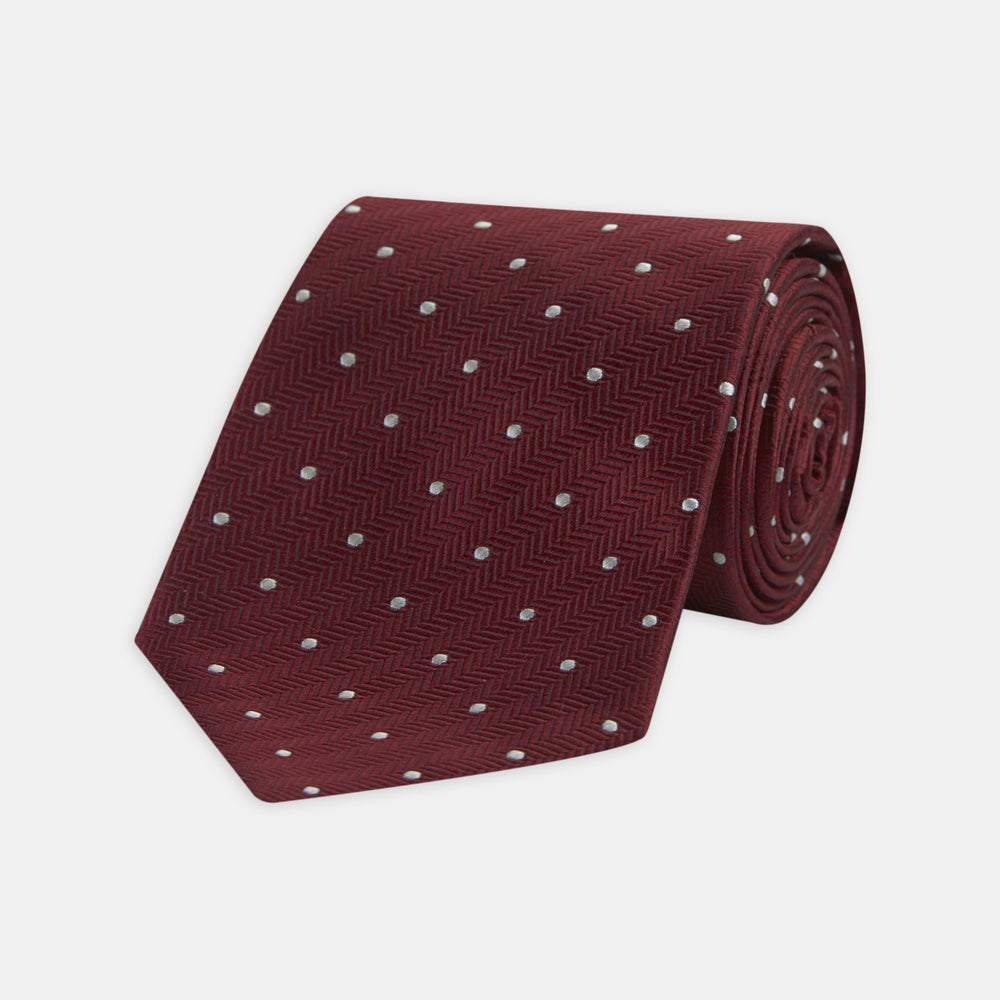 The Turnbull & Asser Burgundy and White Small Spot Herringbone Silk Tie, crafted from fine English silk, is shown rolled up on a plain white background.