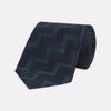 View 1 of product A modern essential, the Turnbull & Asser Navy and Forest Green Striped Zigzag Silk Tie features a bold navy and forest green zigzag pattern, elegantly displayed rolled on a crisp white background.