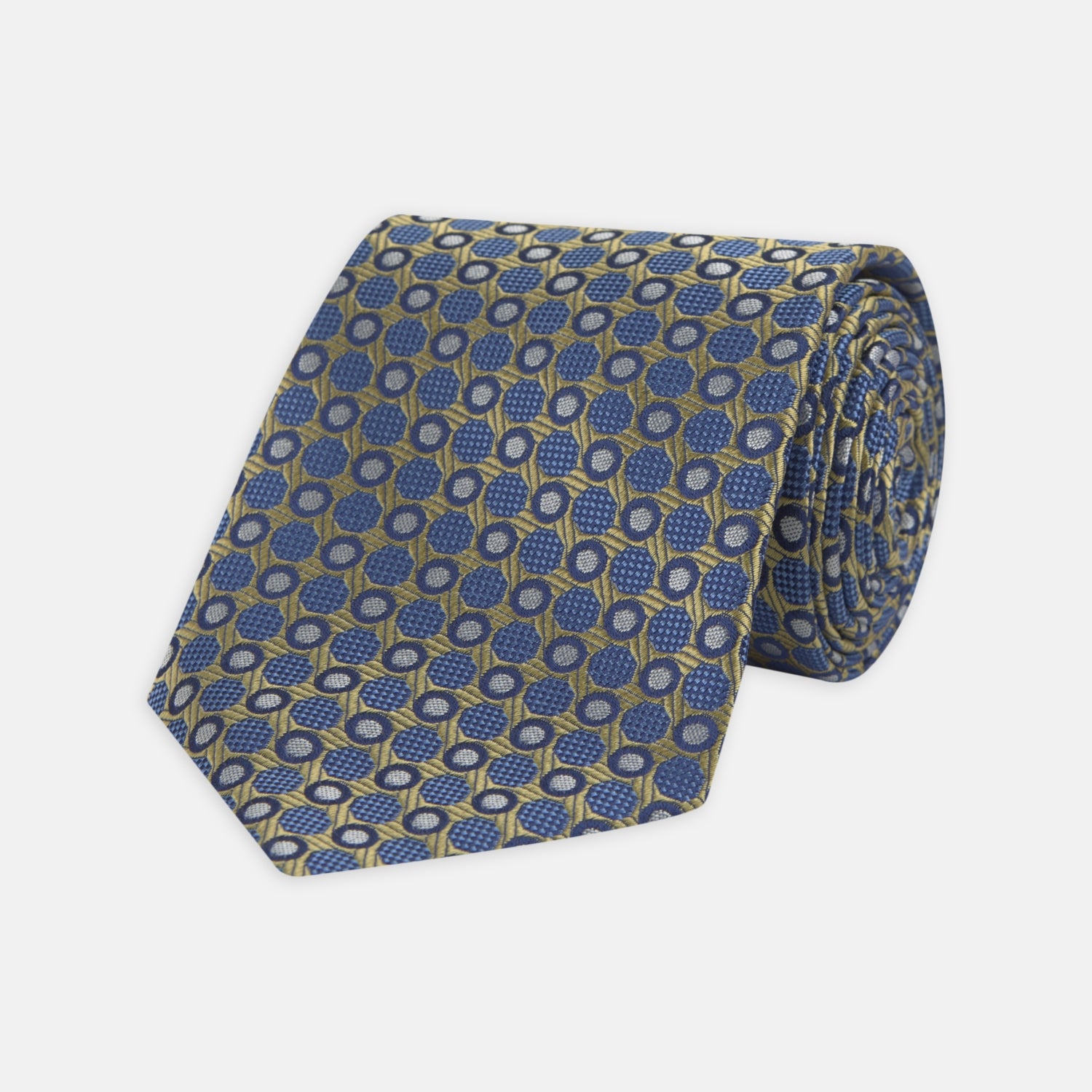 View 1 of product The Gold and Blue Circle and Spot Silk Tie by Turnbull & Asser features blue silk adorned with yellow and white circles and lines, rolled neatly on a light background—an elegant choice for complementing any office shirt.