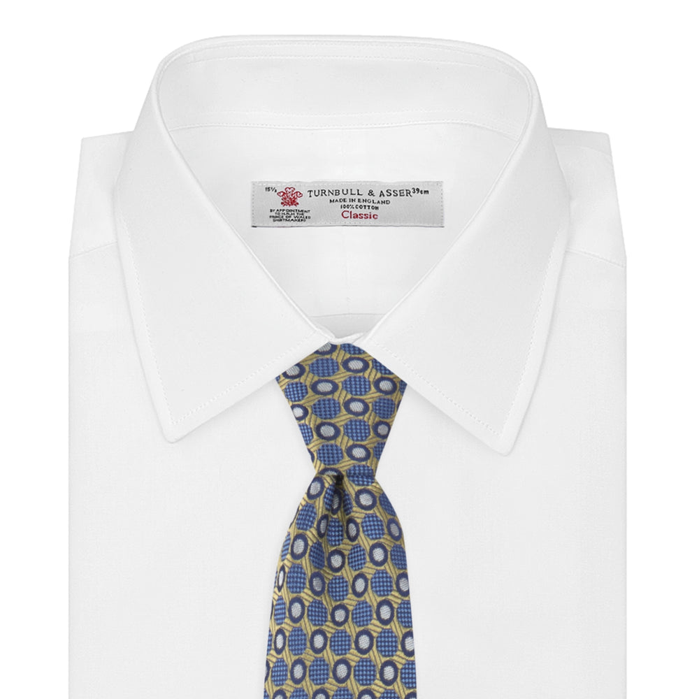The Gold and Blue Circle and Spot Silk Tie by Turnbull & Asser features blue silk adorned with yellow and white circles and lines, rolled neatly on a light background—an elegant choice for complementing any office shirt.