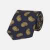 View 1 of product The Turnbull & Asser Navy and Gold Floating Paisley Silk Tie features a repeating yellow and white paisley pattern, shown rolled with the pointed end facing forward against a white background.